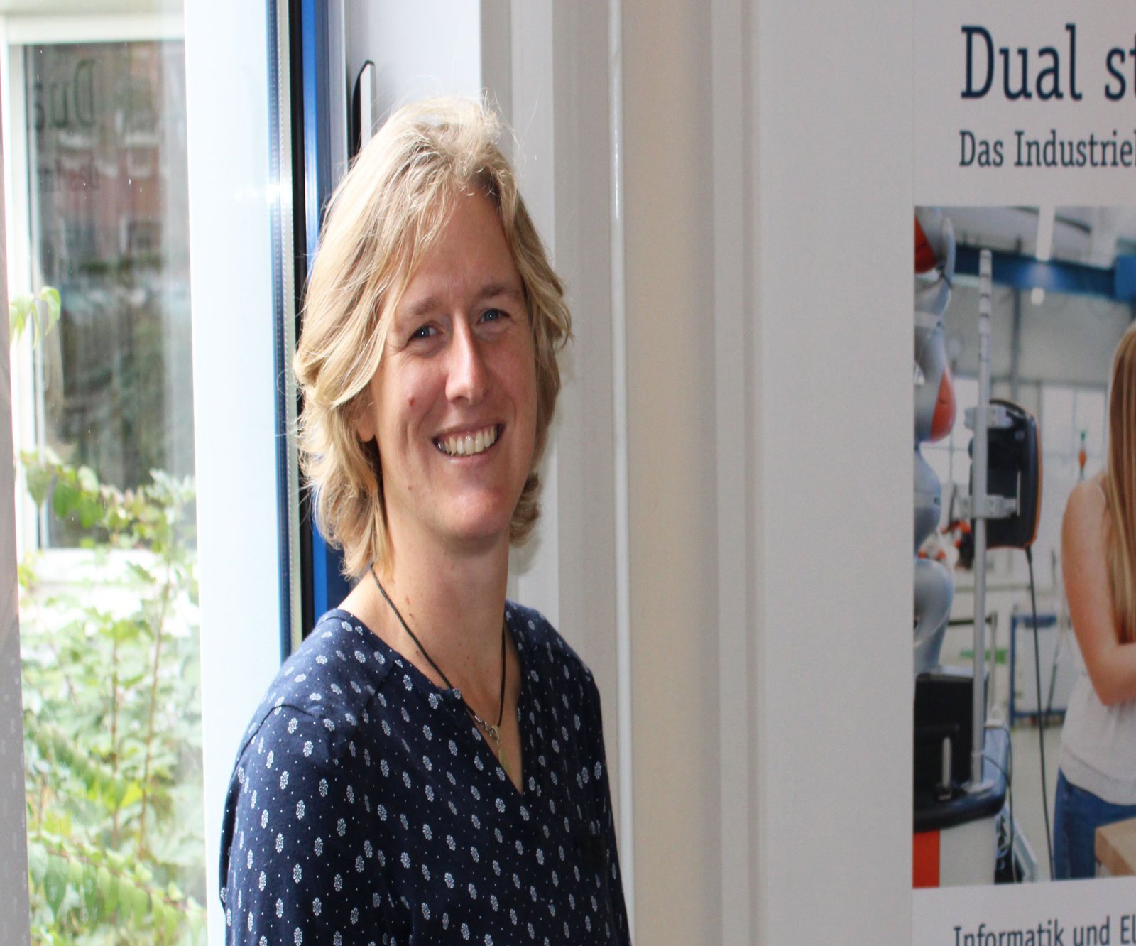 Eine Frau in einer blauen Bluse posiert vor einem Fenster.