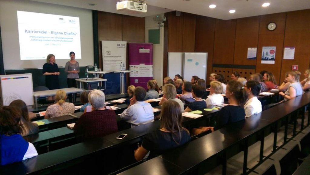 Ein Hörsaal in dem die ersten drei Reihen besetzt sind und das Publikum einem Vortrag beiwohnt.