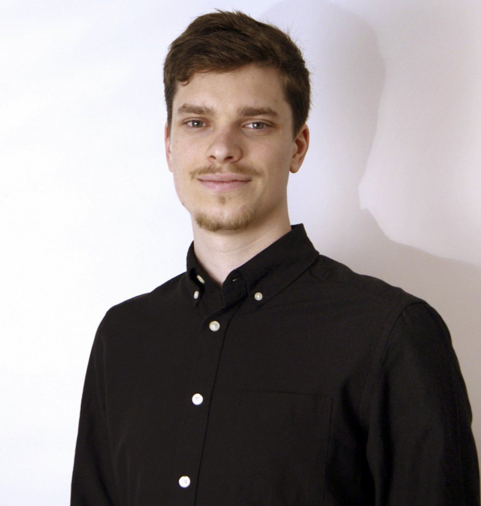 Ein Mann in schwarem Hemd schaut in die Kamera.