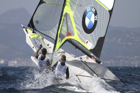 Ein Duo surft auf einem Windsurfer, über die Wellen.