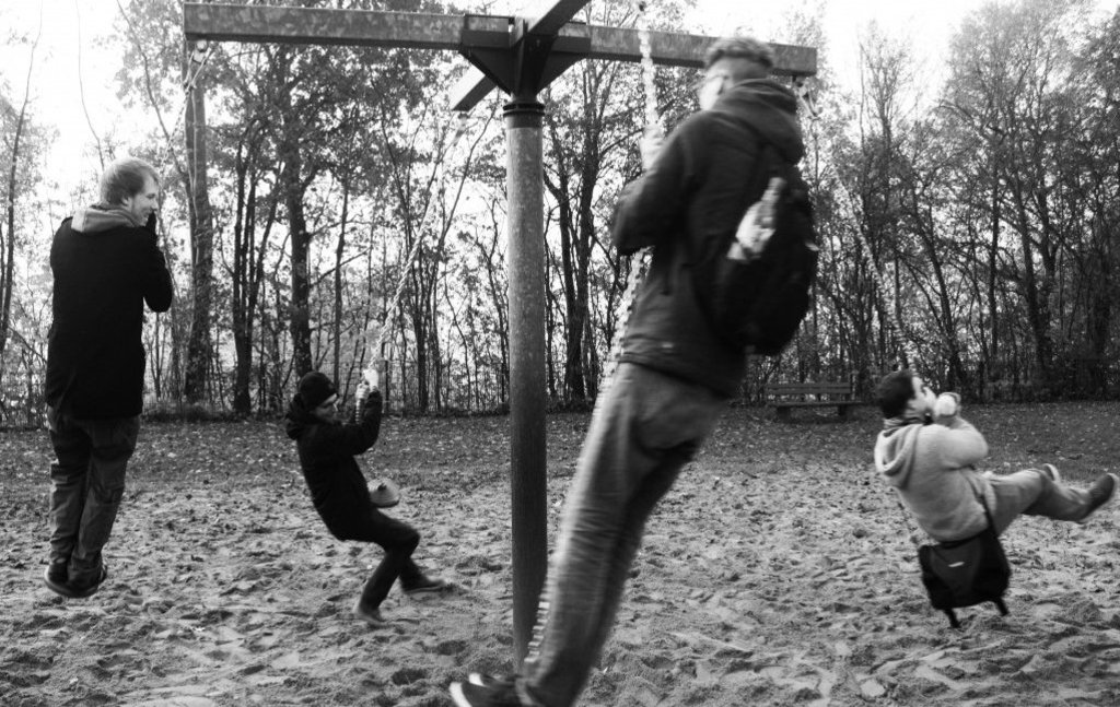 Das Schwarz-Weiß-Bild zeigt vier Männer, die sich auf einer Viererschaukel amüsieren.