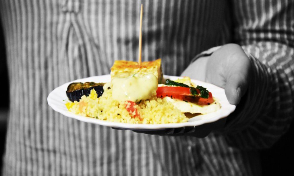 Die Grafik zeigt den Torso einer Person in schwarz-weiß, der Teller mit Häppchen, den die Person hält erstrahlt in knalligen Farben.