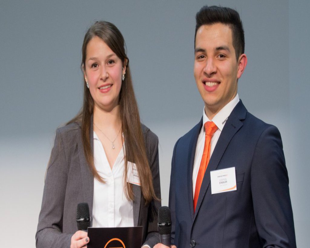 Eine weibliche und ein männlicher Moderator sind mit Moderationskarten und Mikrofonen ausgestattet.