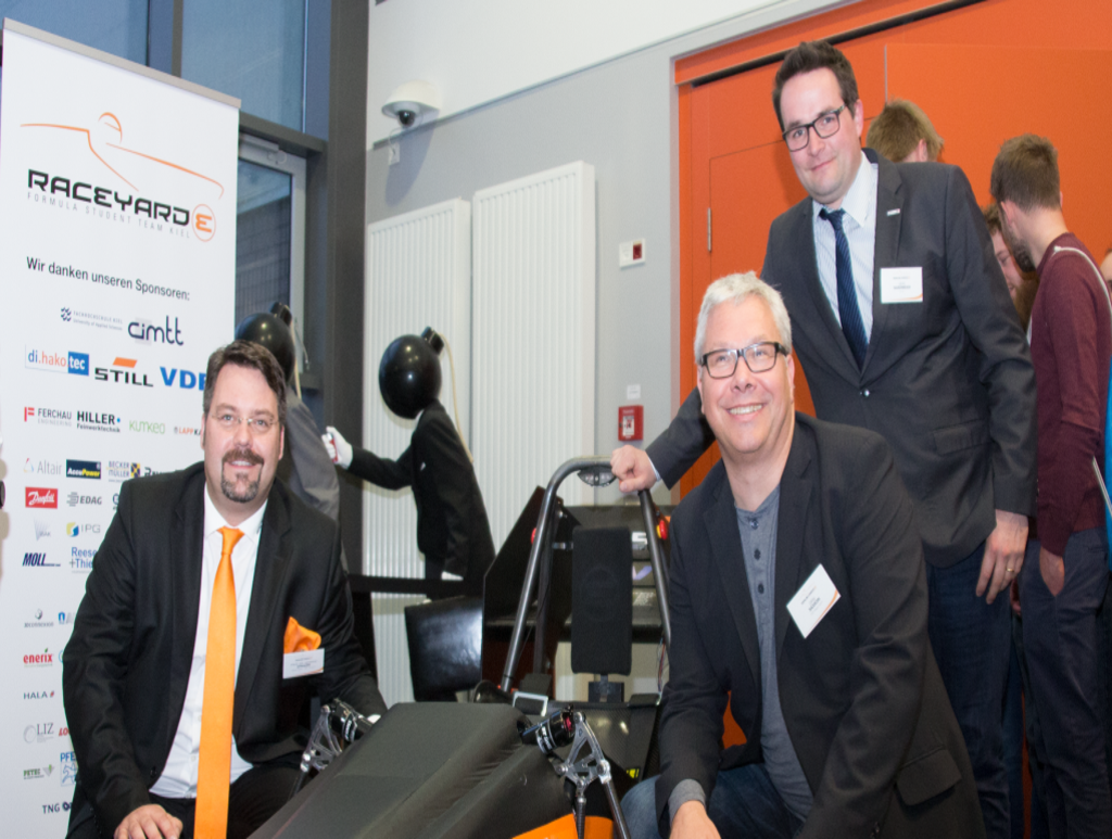 Drei ältere Männer posieren stolz neben einem Rennwagen.