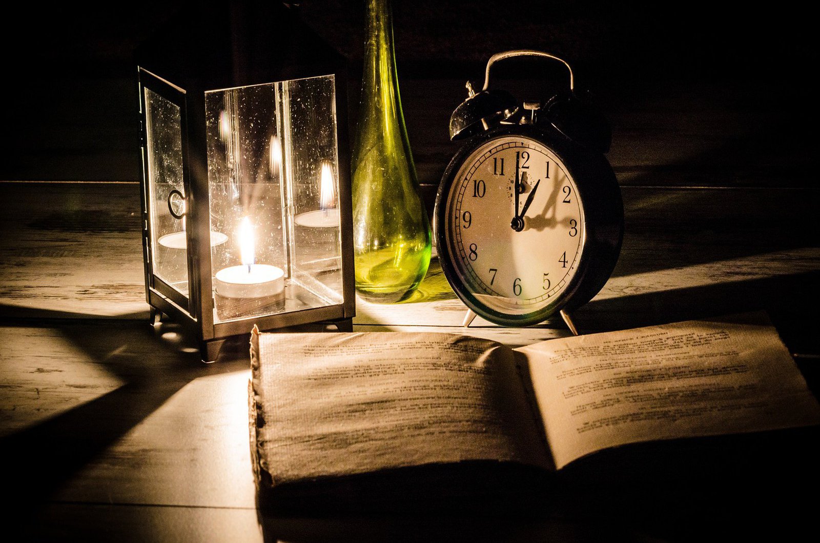 Ein Buch wird beleuchtet von einer Kerzenlampe. Drumherum steht ein Wecker und eine Vase.