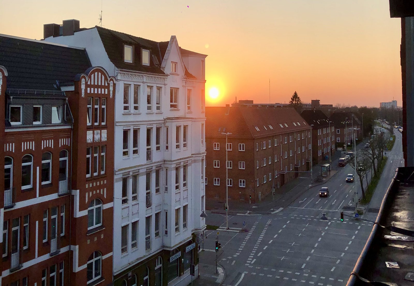 Das Bild zeigt die untergehende Sonne, eingefangen zwischen zwei Wohnhäusern.