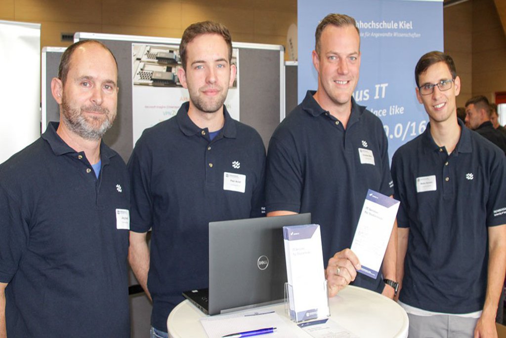 Vier Männer posieren vor ihrem Infostand.