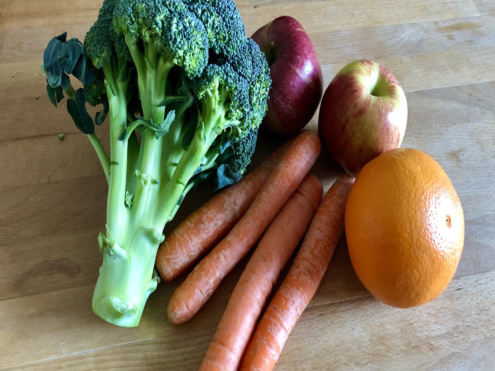 Brokkoli, Äpfel, Karotten und eine Orange auf einem Holztisch.