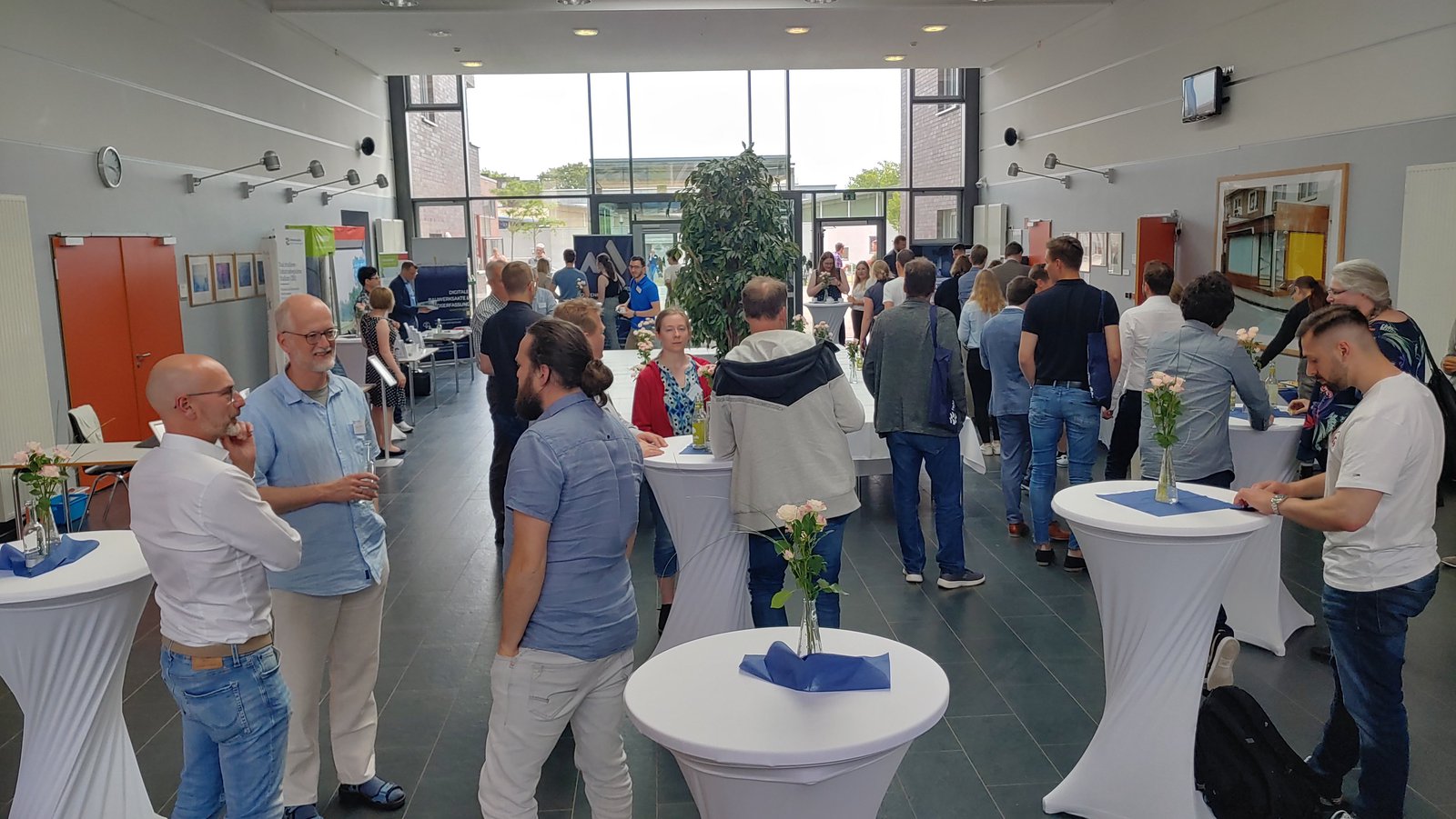 Menschen stehen in einem großen Raum verteilt an Stehtischen.