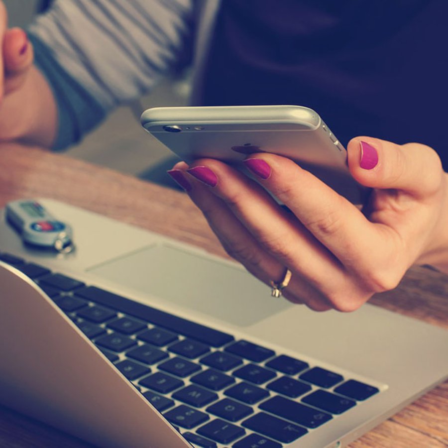Frau vor dem Laptop und mit Handy in der Hand