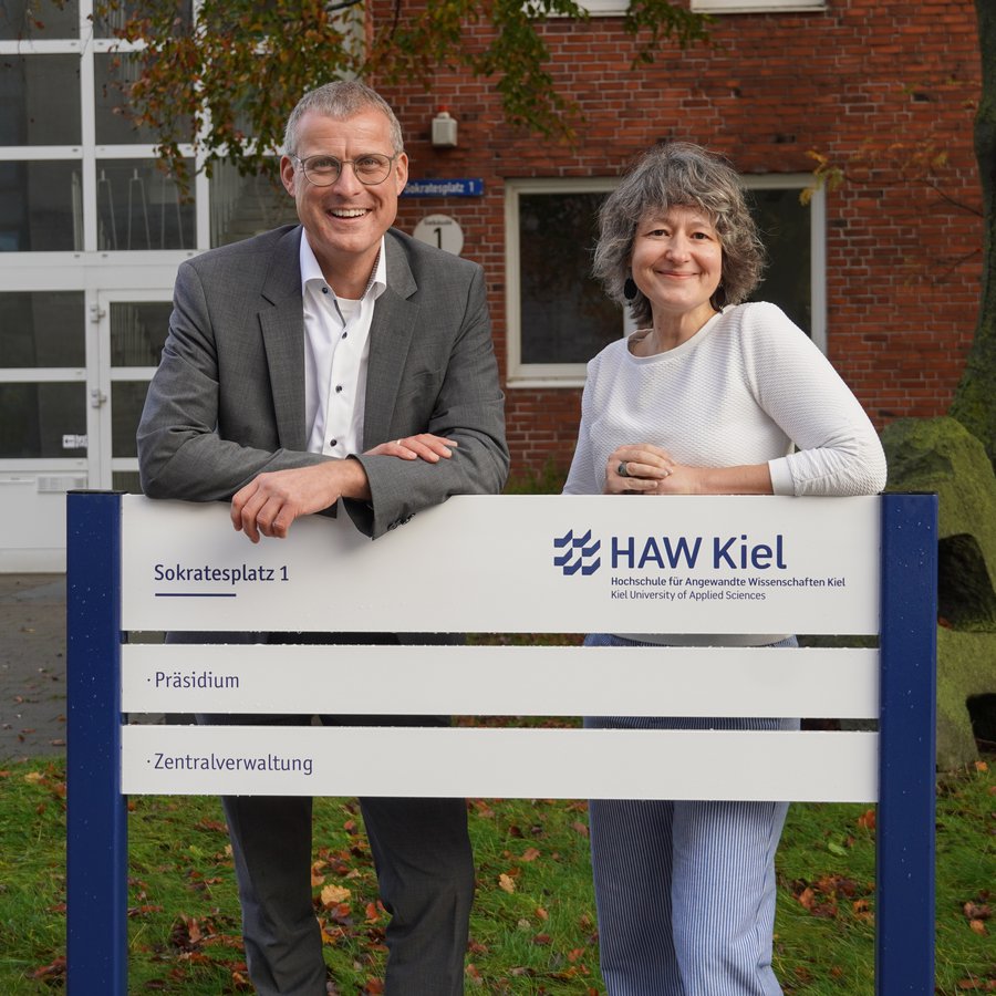 FH Kiel wird HAW Kiel Präsident Prof. Dr. Björn Christensen und Kanzlerin Dr. Anja Franke-Schwenk präsentieren das neue Hinweisschild vor dem Verwaltungsgebäude am Sokratesplatz in Kiel.