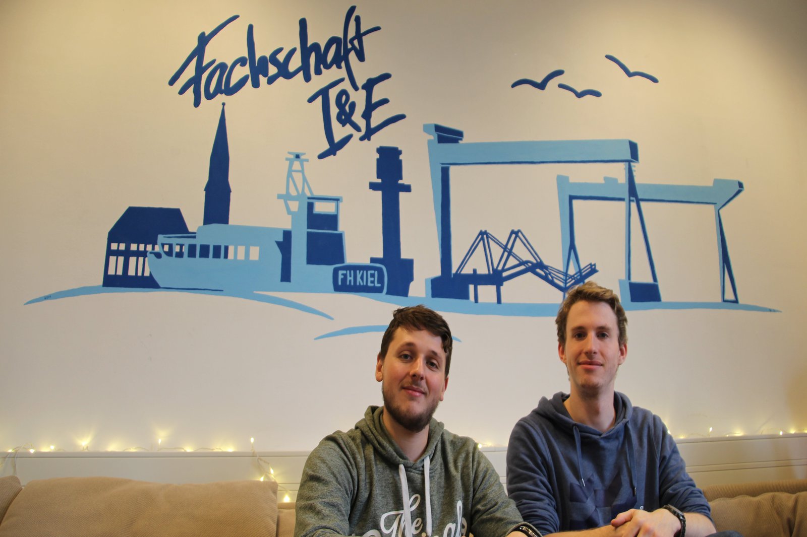 Zwei Männer sitzen auf einem cremefarbenen Sofa, in den Räumen des FB IuE.