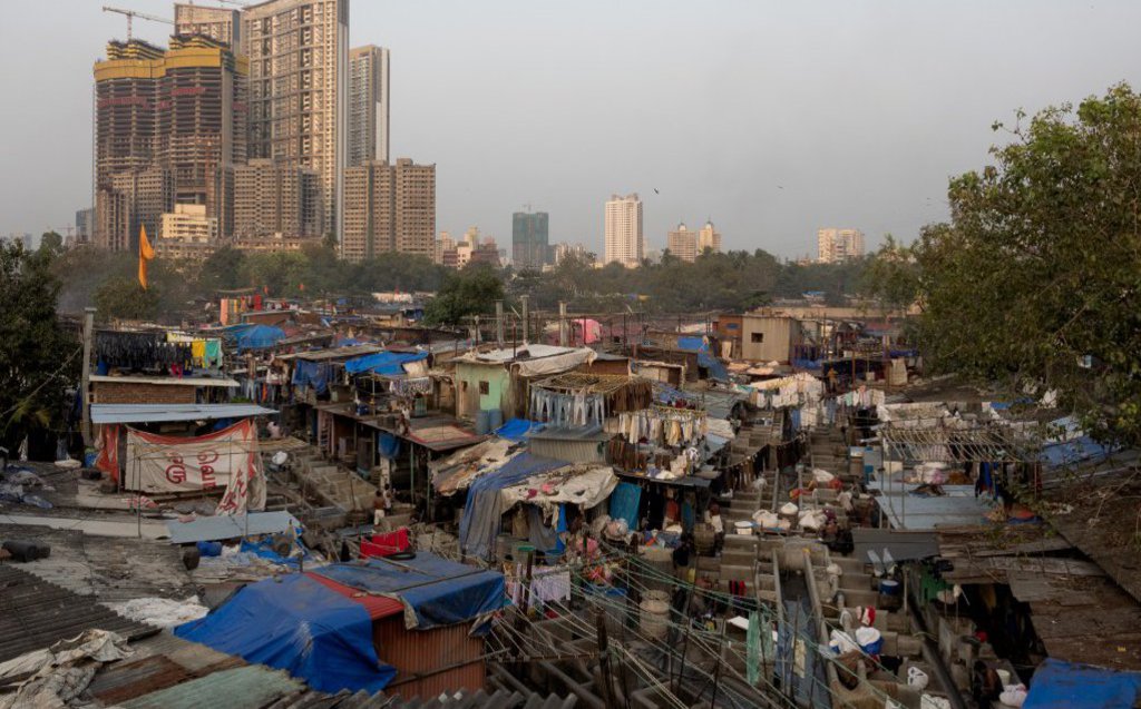 Neben einem Wellblechdorf wird ein Hochhaus gebaut.