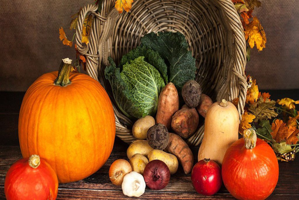 Ein auf der Seite stehender Korb umgeben von verschiedenem Herbst Gemüse.