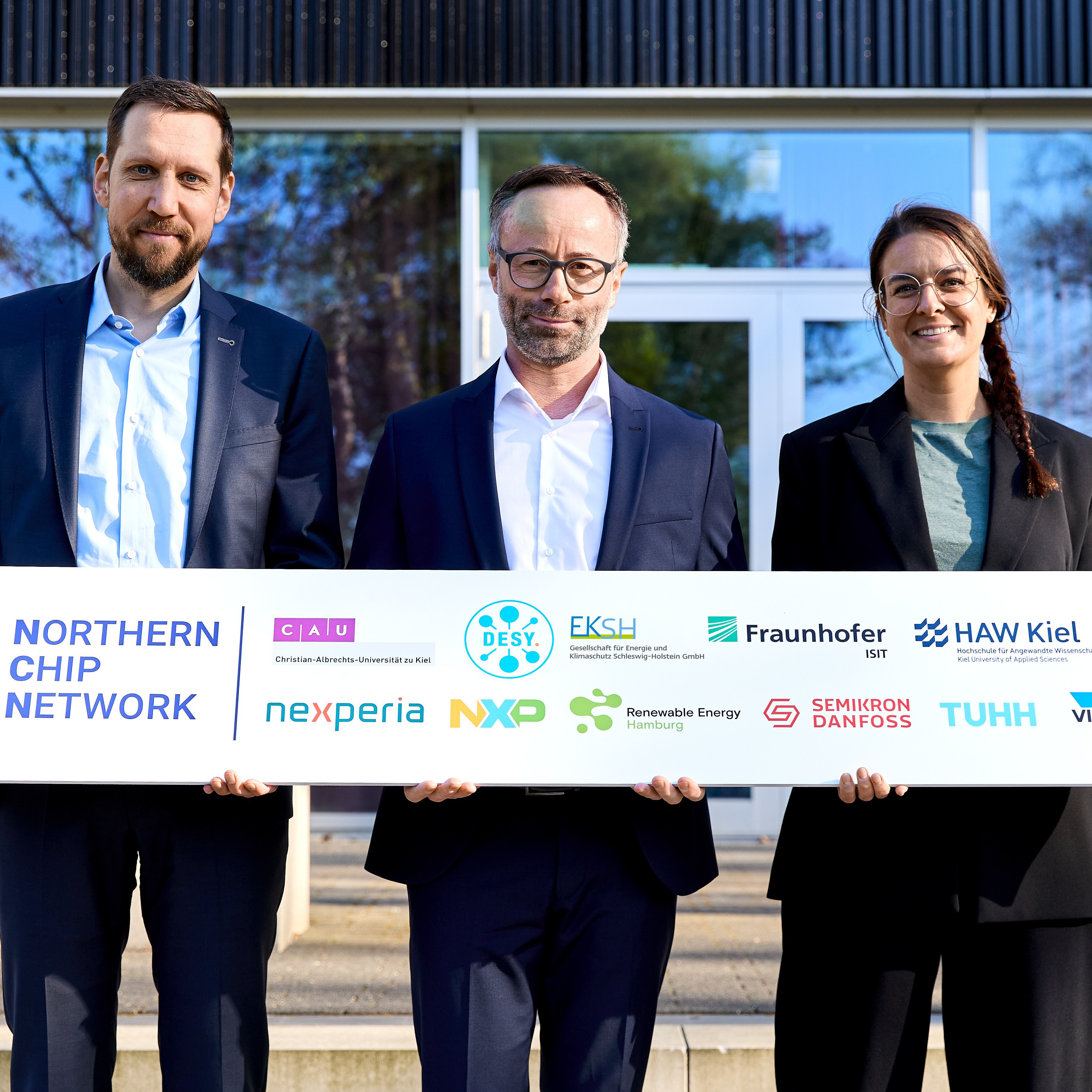 zwei Männer und eine Frau halten ein Schild mit verschiedenen Logos in Händen