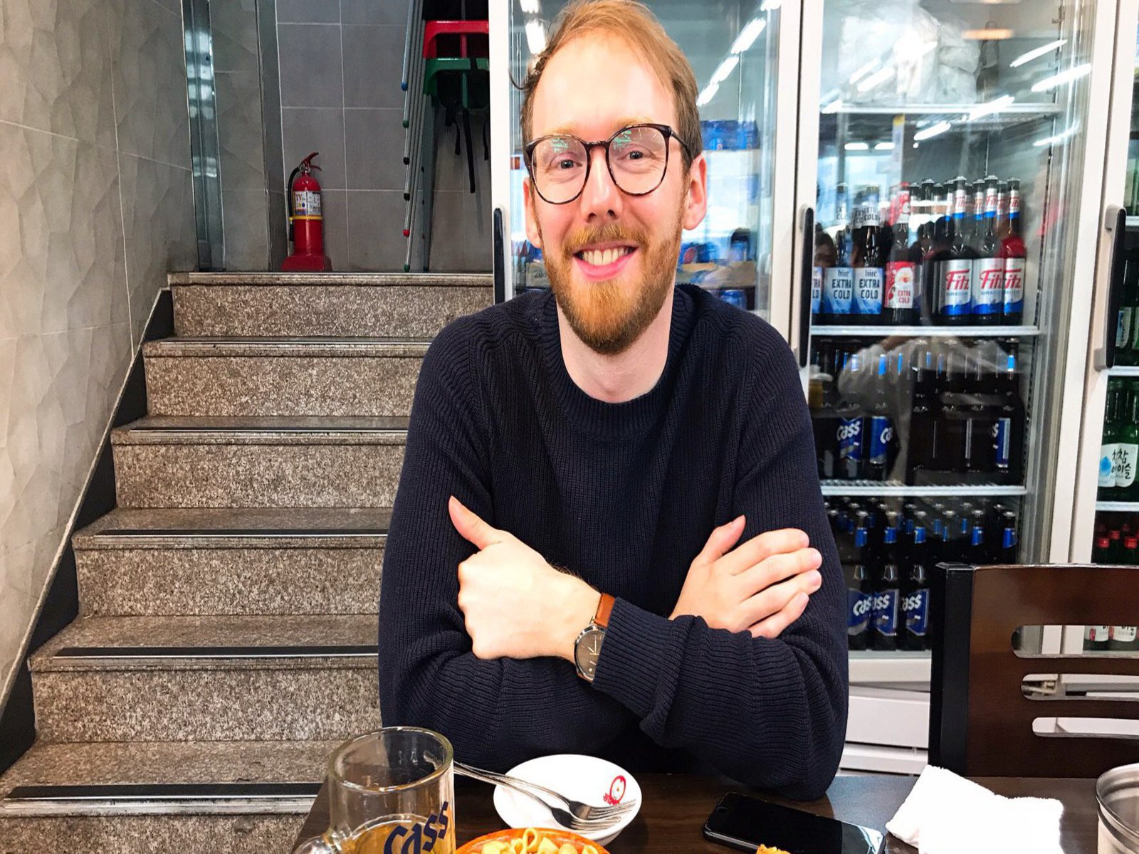 Ein Mann der vor seinen Speisen an einem Tisch sitzt, lächelt zufrieden in die Kamera.