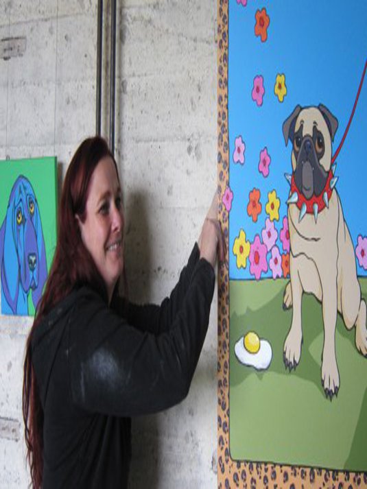 Eine Frau bringt grad zufrieden ein buntes Hundebild an.