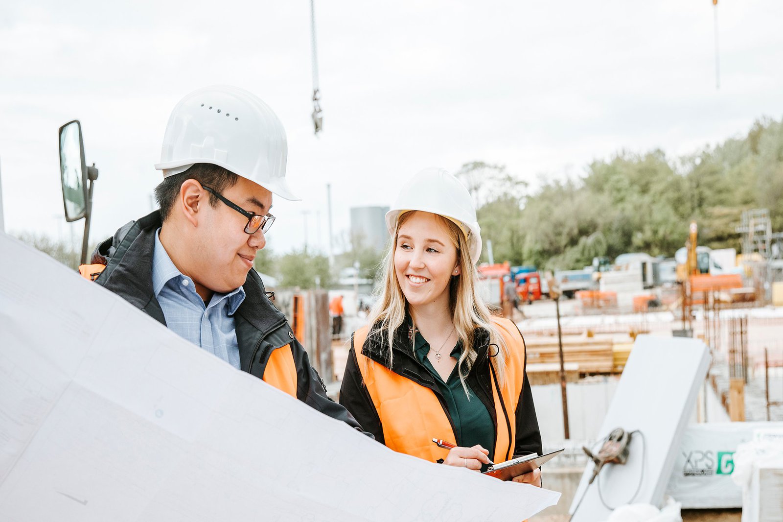 Frau und Mann in Baustellenhelmen und Schutzwesten schauen auf einen Bauplan