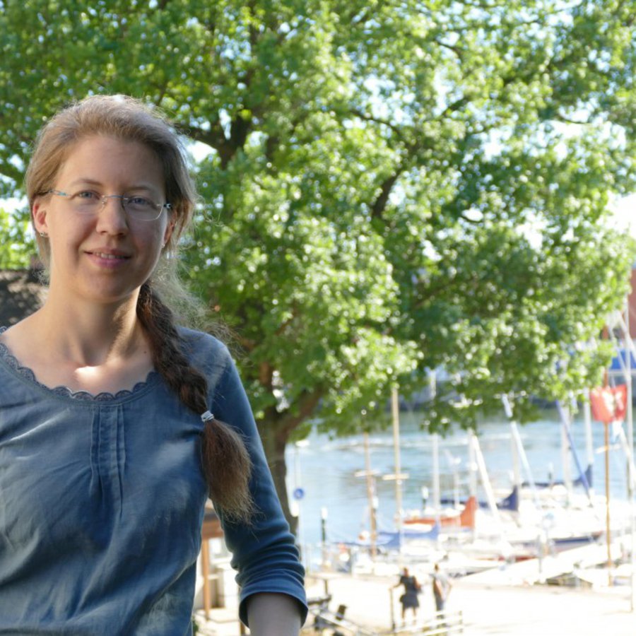 Eine Frau posiert auf einer Anhöhe, im Hintergrund ist unten ein Yachthafen zu sehen.