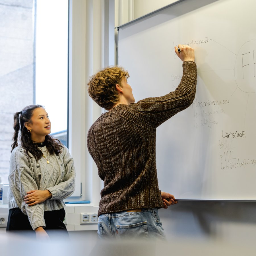 SnowInKiel_2022 ein Mann beschreibt ein Whiteboard, zwei Frauen schauen ihm dabei über die Schulter