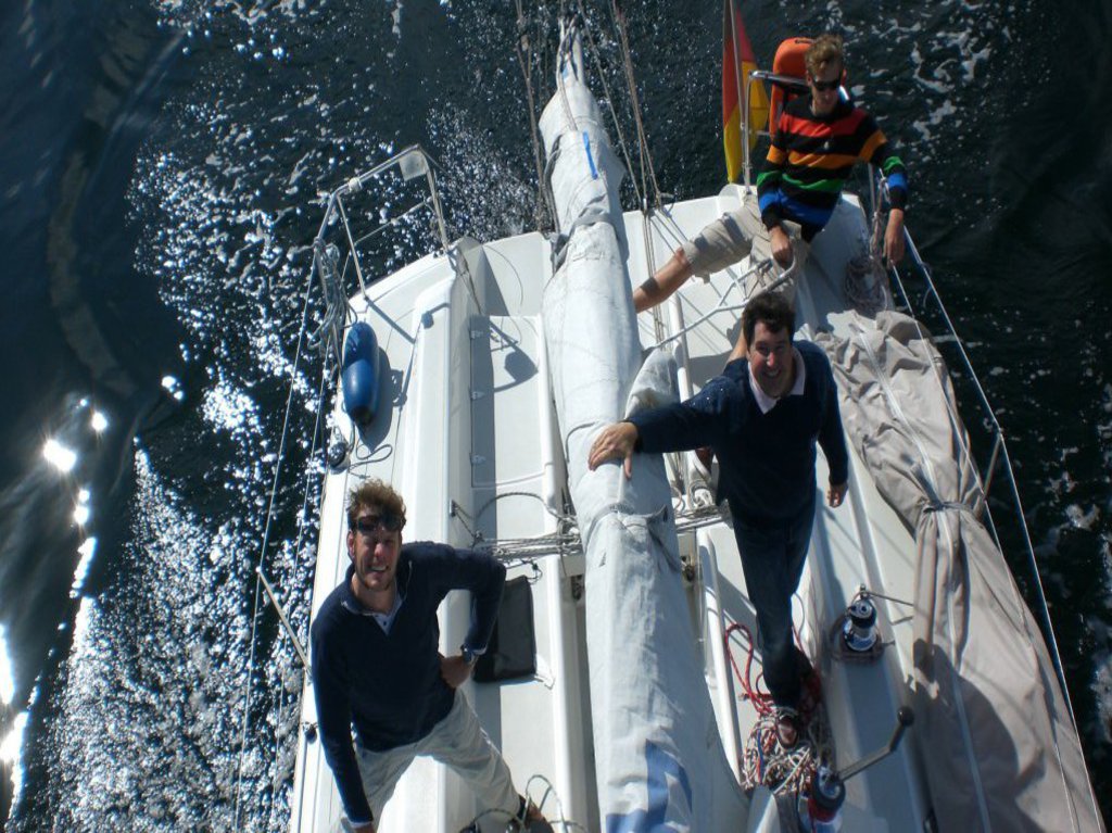 Auf dem Foto sieht man drei Männer, lässig auf einem Segelboot posieren.