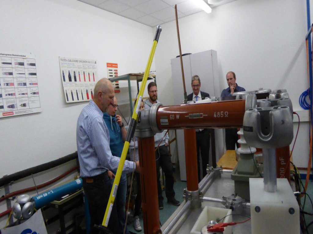 Eine gemischte Gruppe steht in einem Raum und betrachtet eine Maschine.