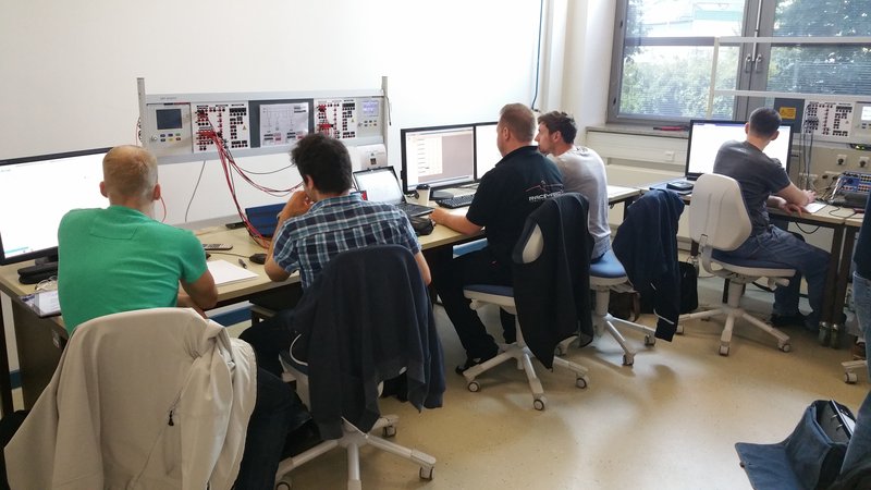 A picture of five student sitting in fron of monitors and laptops to interpret the values of a physical ciruit built up in front of them