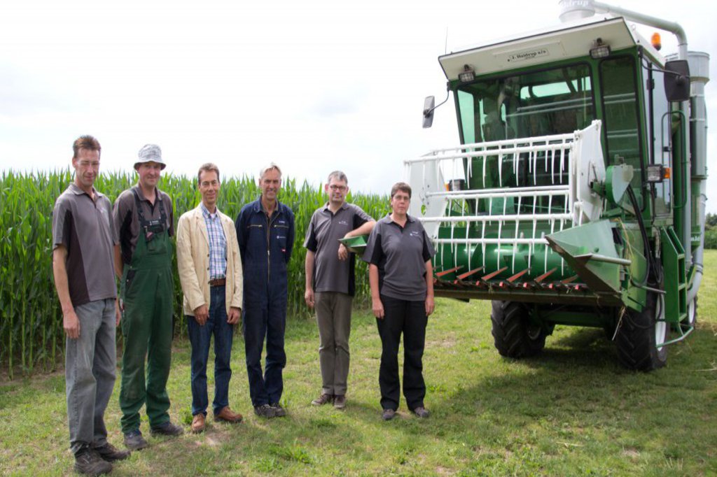 Fünf Männer und eine Frau, stehen auf einem Feld neben einem Traktor.