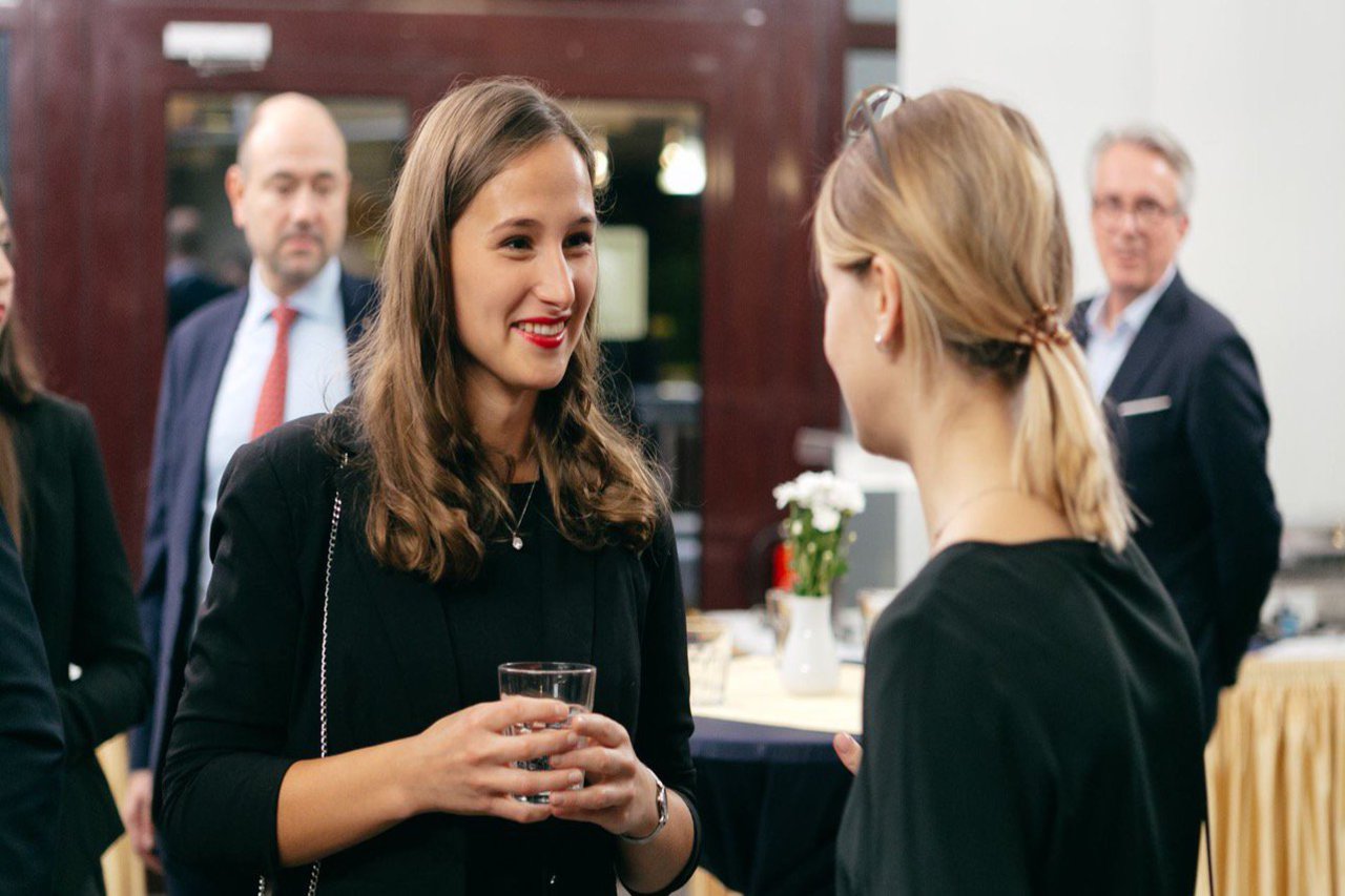 Zwei Frauen unterhalten sich. Im Hintergrund stehen weitere Personen.