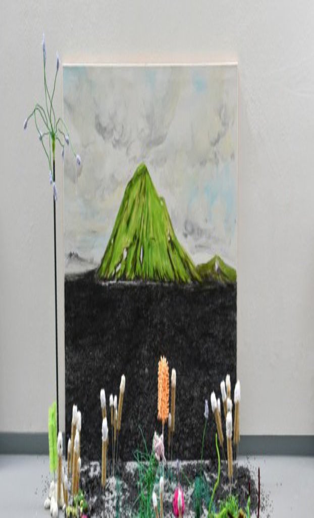 Vor einem auf dem Boden aufgestellten Bild wurde etwas Erde verteilt und künstliche Pflanzen aufgestellt.