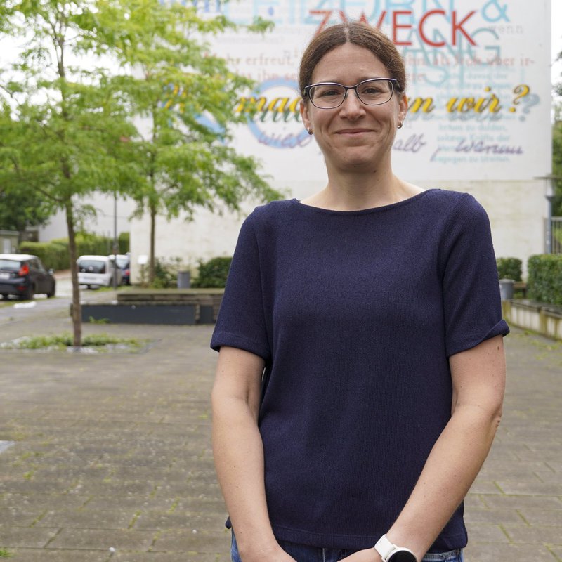 Prof. Dr. Anna Isenhardt steht vor einem Wandgemälde auf dme Campus der FH Kiel. 