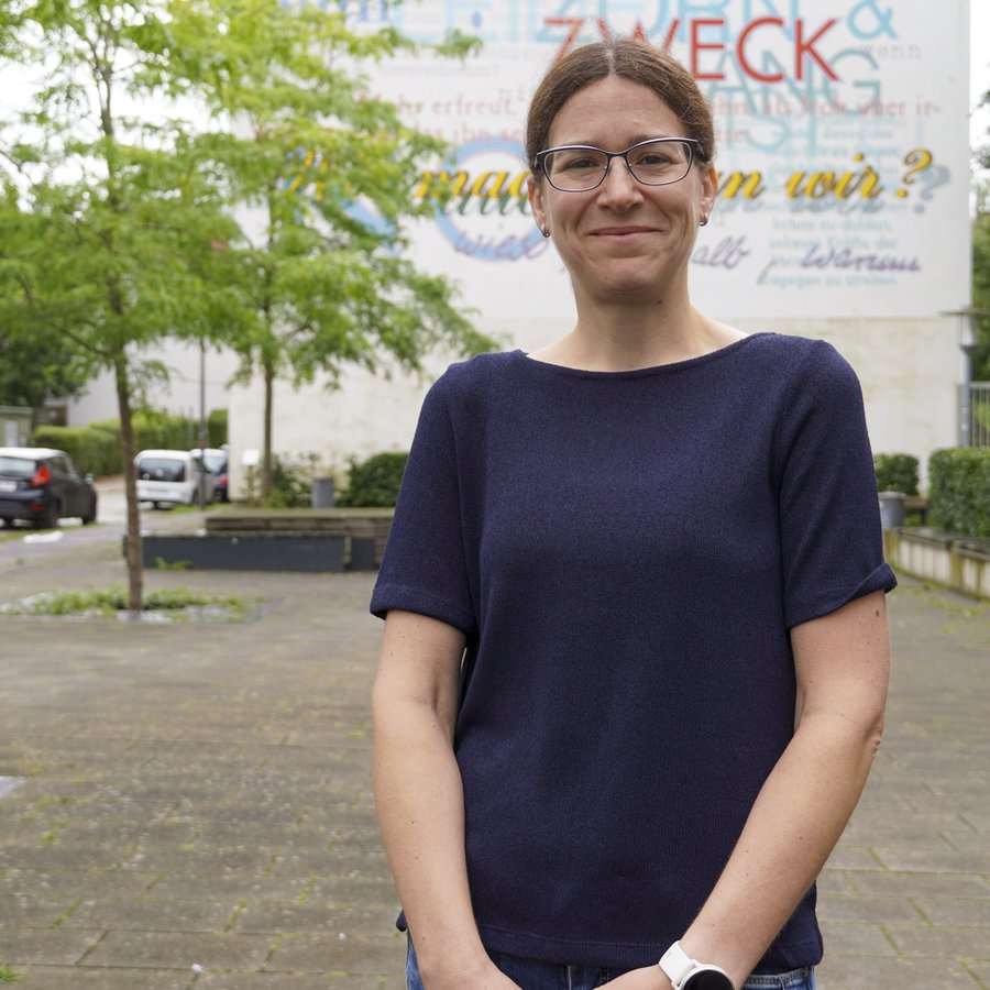 Prof. Dr. Anna Isenhardt steht vor einem Wandgemälde auf dme Campus der FH Kiel.