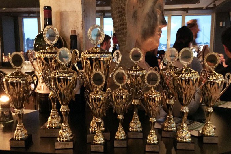 Viele Pokale stehen auf einem schwarzen Regal.