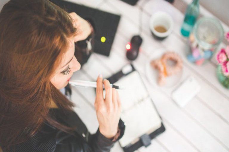 Eine Frau lehnt grübelnd über ihrem Schreibtisch und den darauf liegenden Utensilien.