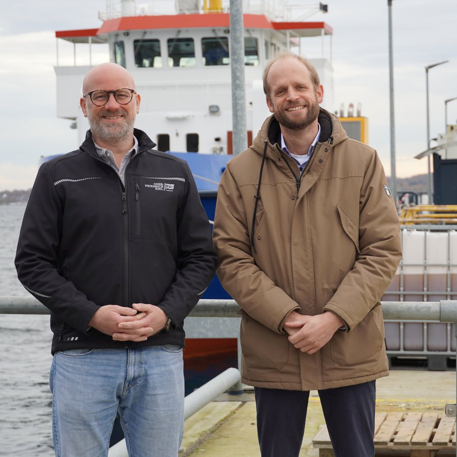 Zwei Männer stehen auf de Kai der Kieler Gebr. Friedrich Werft: Sönke Stich (links) und Prof. Dr.-Ing. Hendrik Dankowski von der HAW Kiel