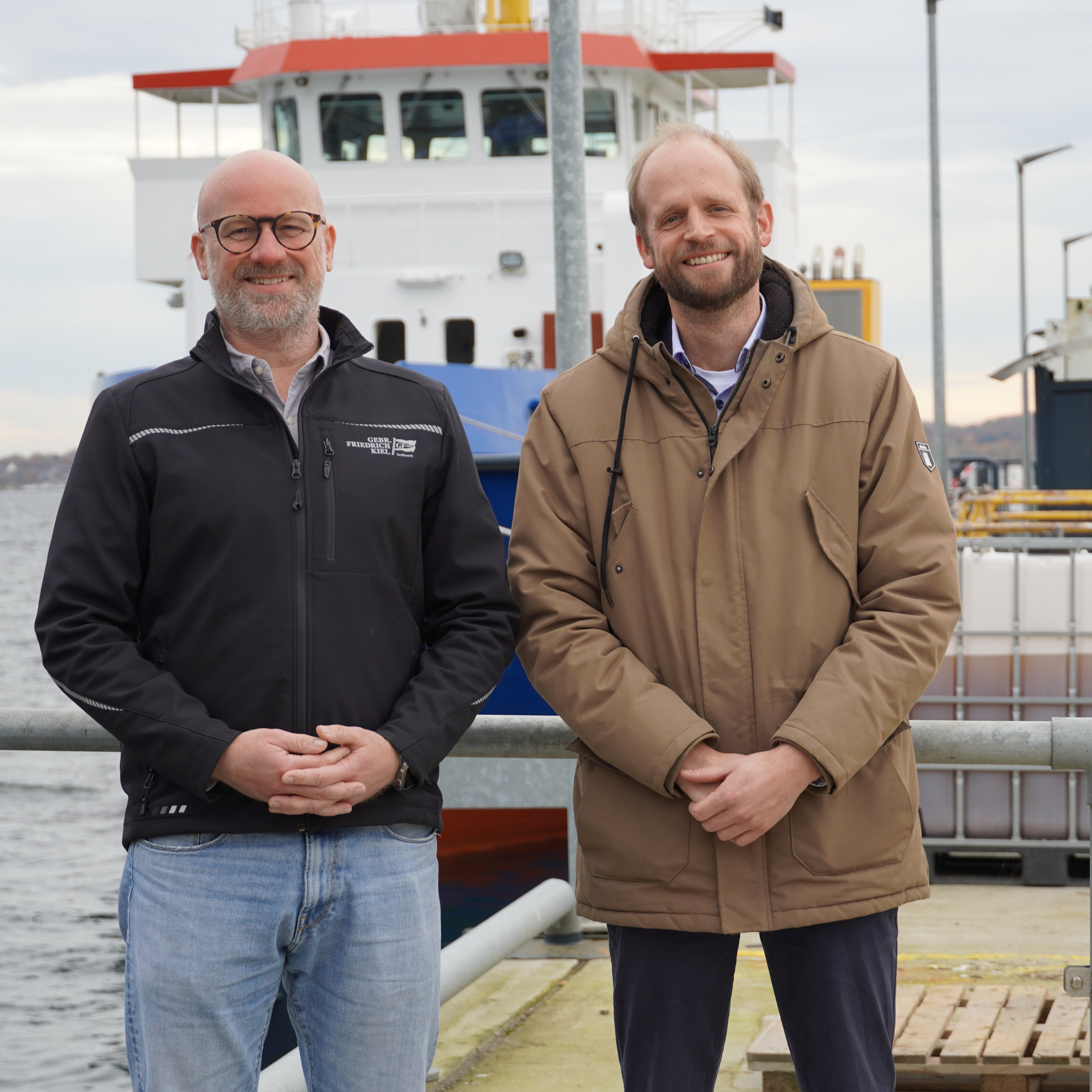 Zwei Männer stehen auf de Kai der Kieler Gebr. Friedrich Werft: Sönke Stich (links) und Prof. Dr.-Ing. Hendrik Dankowski von der HAW Kiel 