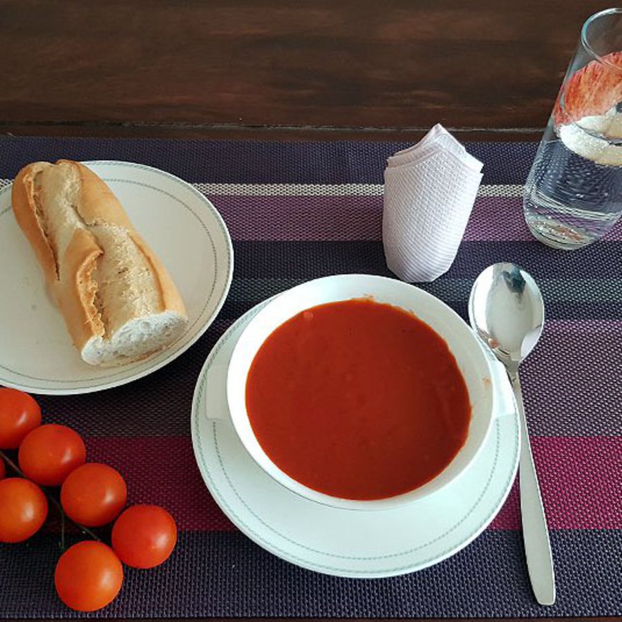 Tomatensuppe, Baguette und Cherrytomaten, liegen auf einem Holztisch bereit.