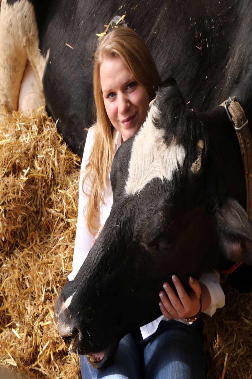 Nina Zingelmann angeschmiegt an eine Kuh, die im Stroh liegt.