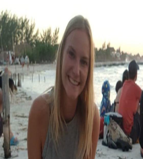 Eine Frau lächelt sitzend am Strand.