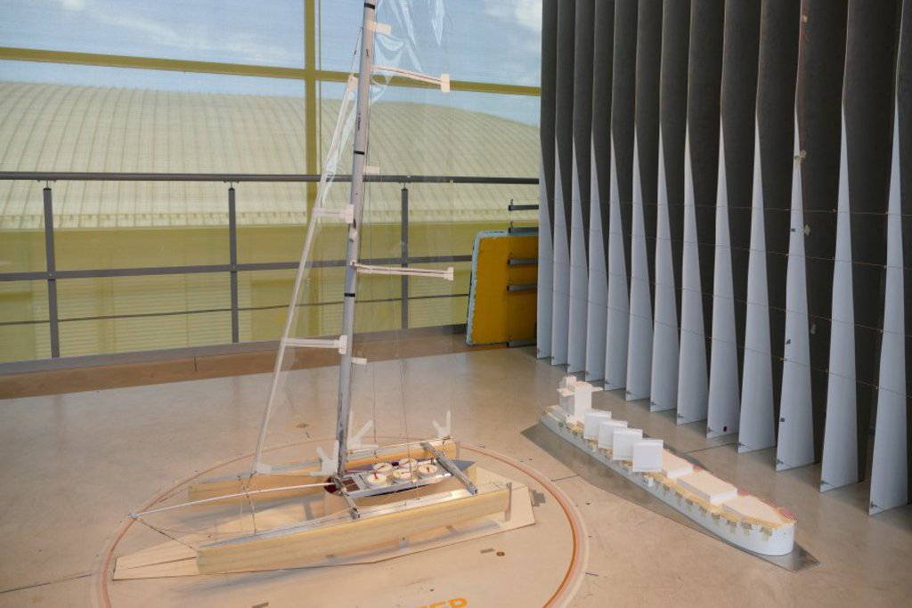 Ein verhältnismäßig großer Katamaran und ein Frachtschiff liegen in einem Windsimulator.