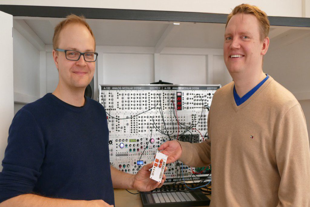 Zwei Männer stehen vor einem Schaltkasten und lächeln freundlich in die Kamera.