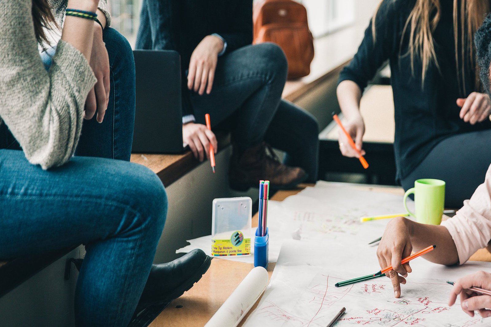 Eine Gruppe Stidierender sitzt mit Stiften bewaffnet um ein großes Skizzenpapier.
