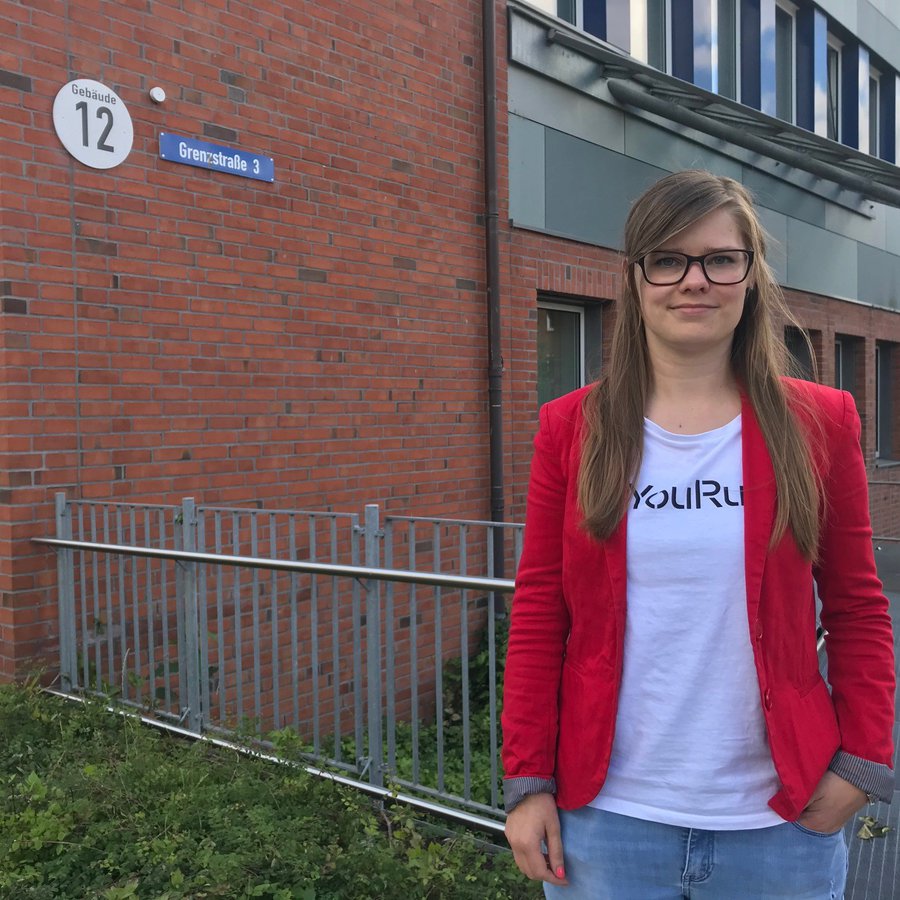 Foto: Meise Eine junge Frau in rotem Blazer steht vor dem Gebäude des Fachbereichs Medien.