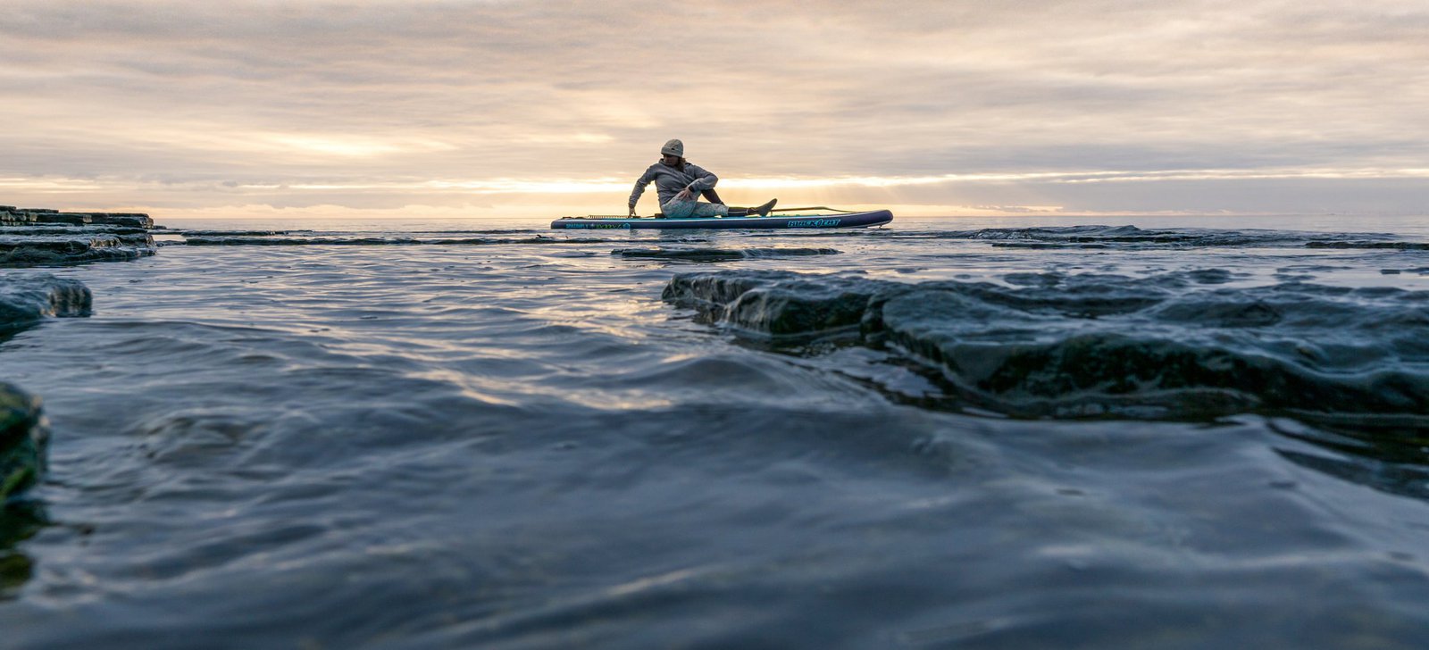 Ein Mann dehnt sich auf einem, auf dem Wasser treibenden Supboard.