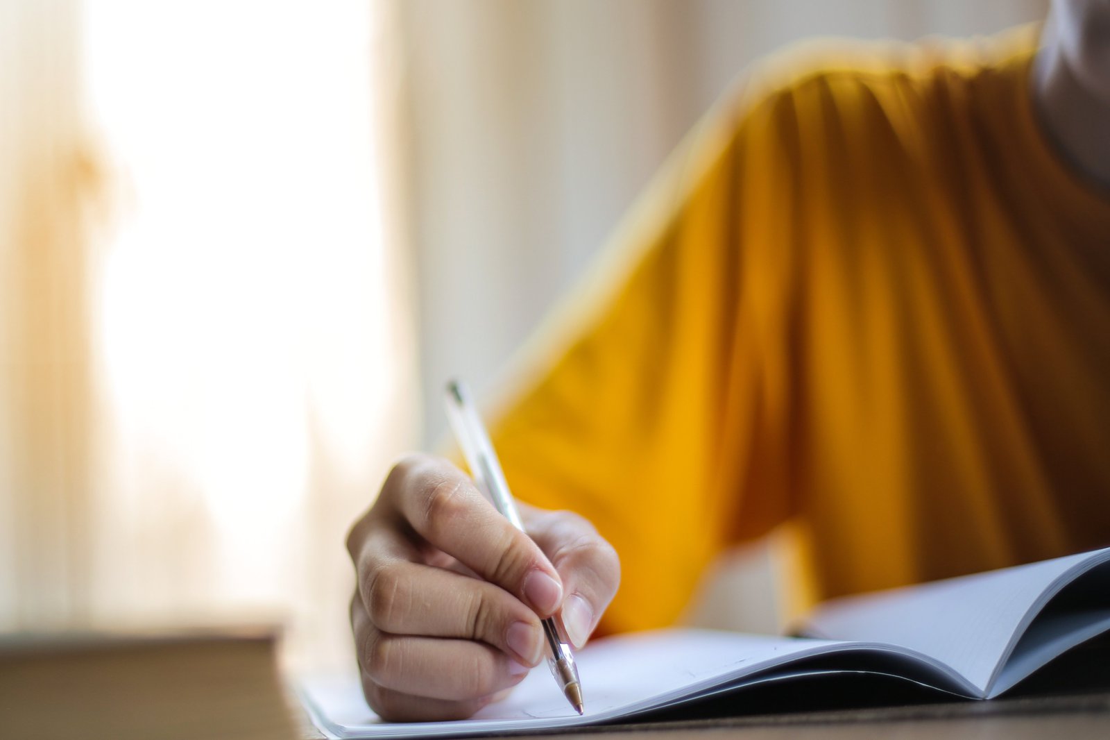 Schulter und Hand einer Person, die etwas in ein Heft schreibt