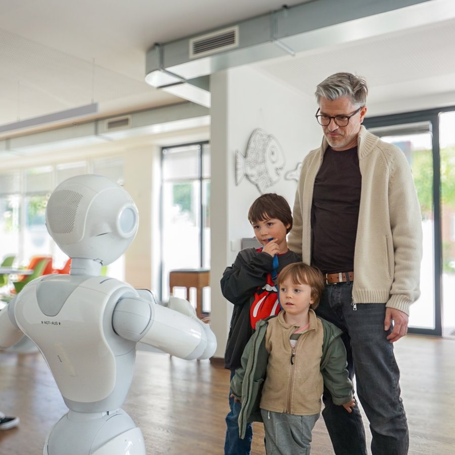 Ein Vater mit seinen Söhnen schauen sich ein Roboter an.