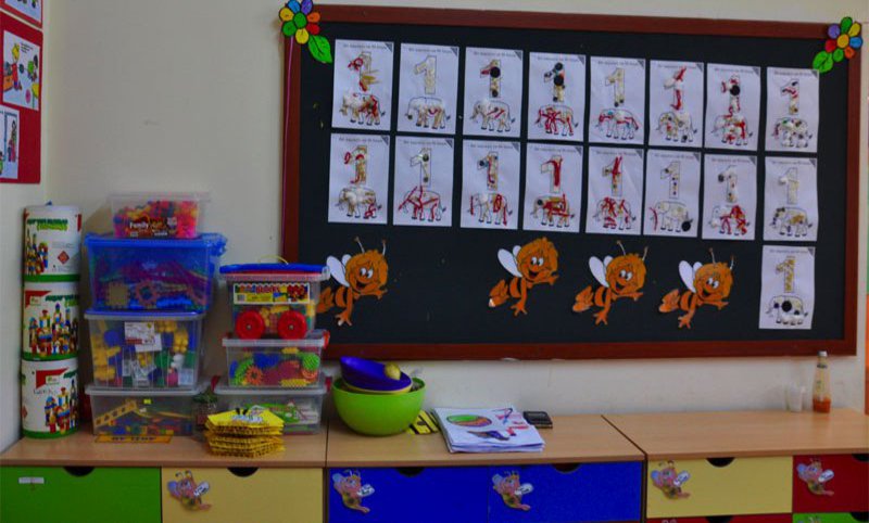 An einer Wand hängt ein Holzboard mit Basteleien von Kindern. Darunter und daneben finden sich Kästen mit Spielzeug.