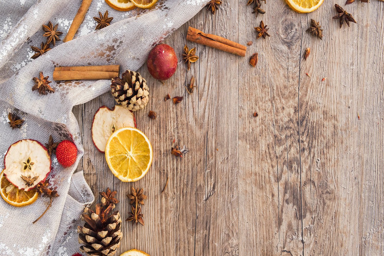 Ein mit Zimtstangen, Apfelscheiben, Nelken und Orangenscheiben geschmückter Holztisch.