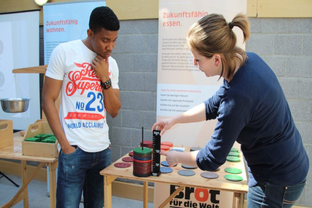 Ein Mann und eine Frau stehen an einem Infostand von "Brot für die Wel"t und messen etwas ab.