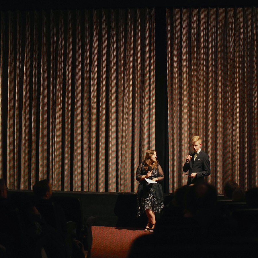 Zwei Personen vor einem geschlossenen Bühnenvorhang